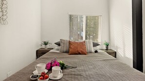 Un dormitorio con cama, mesitas de noche, una ventana con persianas y una zona de desayuno en la cama.