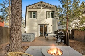 Una casa de dos pisos con terraza, un brasero, asientos al aire libre y una parrilla.