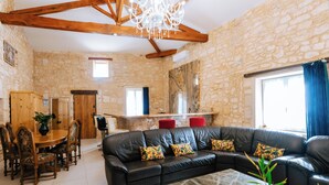 A spacious living area with a black leather sofa, wooden dining table, and chairs, stone walls, and a chandelier. - Gîte Marianne au Domaine Pagnon Gironde: quiet, heated swimming pool near Bordeaux (Saint-Gervais)