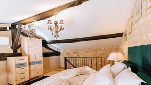 A bedroom with a wooden wardrobe, a bed with patterned bedding, a chandelier, and a stone wall. - Gîte Marianne au Domaine Pagnon Gironde: quiet, heated swimming pool near Bordeaux (Saint-Gervais)