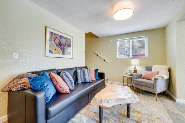 A living room with a black leather sofa, a wooden coffee table, a gray armchair, and a colorful rug.