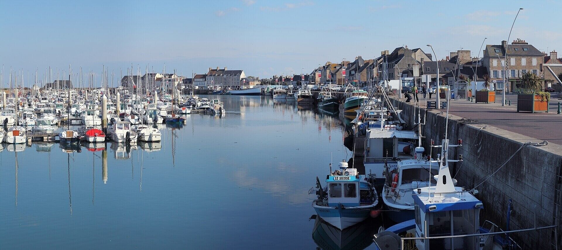 A marina with boats docked along a waterfront, buildings in the background, and a clear sky.