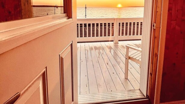 A room with a view of the sunset over the ocean, a wooden deck, and a window with a map.