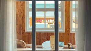 A room with a large window overlooking a wooden deck and a beach.