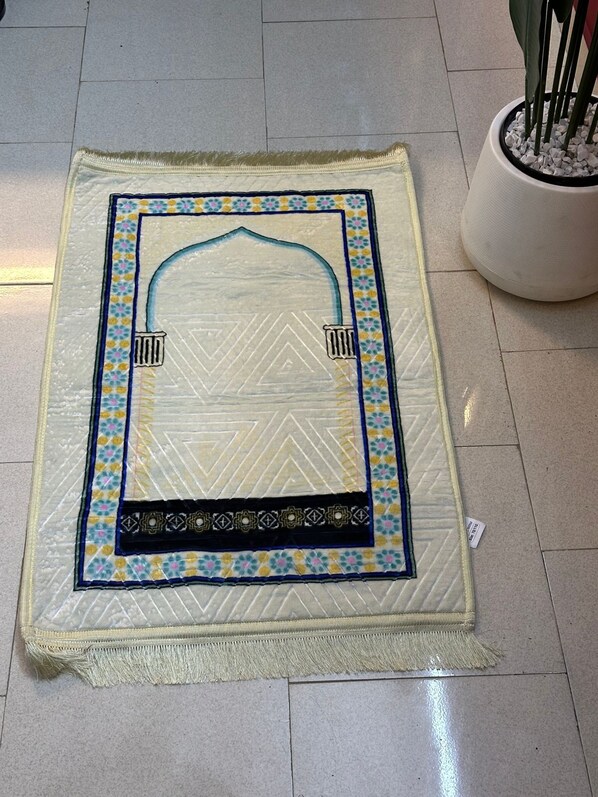 Una alfombra de oración con un diseño geométrico y un arco central, sobre un suelo de baldosas.