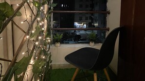 A small balcony with a chair, string lights, and potted plants.