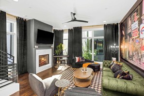 A modern living room with a fireplace, a flat-screen TV, a green sofa, and a checkered rug. - Sleeps 24! Broadway Views, Rooftops & Karaoke (Nashville)