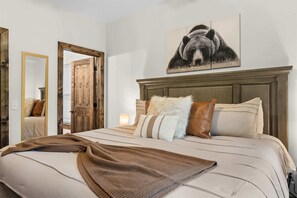 Ein Schlafzimmer mit einem Bett, Kissen, einer Decke, einem Spiegel und einem an der Wand hängenden Bild.