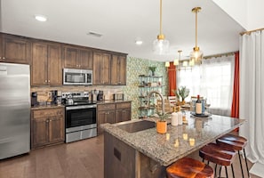 A modern kitchen with wooden cabinets, stainless steel appliances, a granite countertop, and a central island with bar stools.