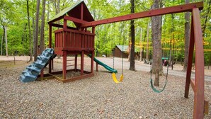Un'area giochi con uno scivolo in legno e altalene, immersa nel verde.