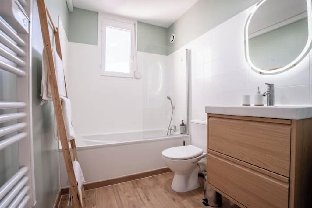 Un bagno con vasca, servizi igienici e un mobiletto contenitore in legno con specchio.