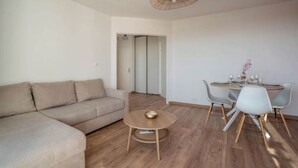Una sala de estar moderna con un sofá beige, una mesa redonda de centro y una zona de comedor con mesa y sillas.
