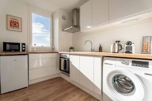 A compact kitchen with a washing machine, a microwave, and a small refrigerator. - T2 air-conditioned Private parking Balcony Autonomous arrival (Villefranche-sur-Saône)