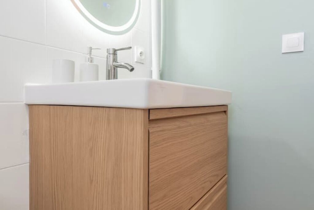 A bathroom with a white sink, wooden cabinet, and a round mirror above the sink.