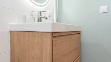 A bathroom with a white sink, wooden cabinet, and a round mirror above the sink.