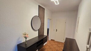 A hallway with a dark wooden console table, a round mirror, and a decorative vase with flowers. - 70m² suite incl. 98 "Smat-TV + parking lot + balcony (Chemnitz)