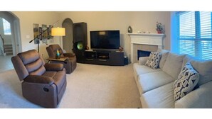 A living room with a sofa, two recliners, a TV, a fireplace, and a lamp.