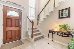 A wooden front door with a glass panel, a staircase with white railings, and a small table with a clock and plants. - World Cup Hub 4 mile drive to NRG Stadium or ride Metro Rail (Houston)