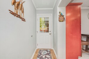 A hallway with a white door, a red wall, and a wooden bench. - Coco Cottage: Dog-Friendly Bungalow in Quiet, Walkable Neighborhood (Oak Island)