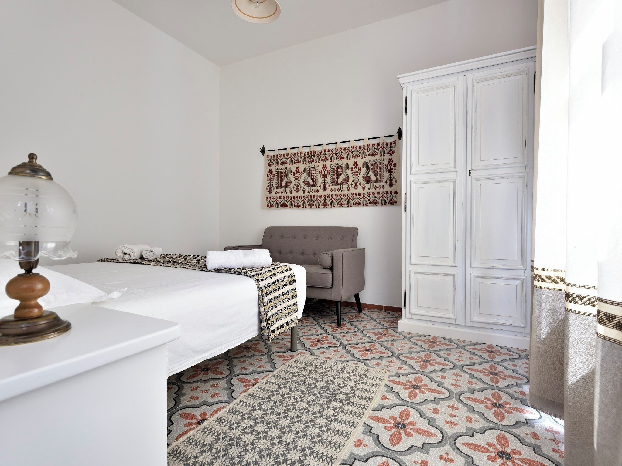 A bedroom with a bed, a chair, a wardrobe, and a patterned rug.