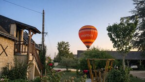A hot air balloon with 'smartbox' written on it, flying over a residential area with houses, a garden, and a wooden structure. - Gîte Le Laurier (Villebernier)