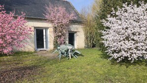 A stone house with a grassy yard, a table with chairs, and flowering trees. - Gîte Le Laurier (Villebernier)