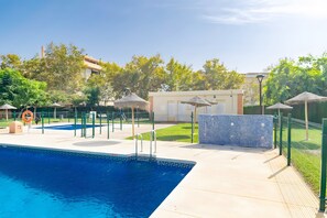 Ein Swimmingpool mit klarem, blauem Wasser, umgeben von einem eingezäunten Bereich, mit einem Gebäude im Hintergrund.
