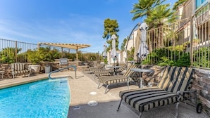 Un espace aménagé au bord de la piscine, avec des chaises longues et des parasols, une pergola et un mur en pierre.