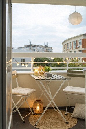 Een balkon met een tafeltje, twee stoelen, lichtslingers en een hanglamp.
