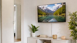 Un saló modern amb televisió plana penjada a la paret, un moble blanc d'entreteniment amb objectes decoratius, una catifa amb dibuixos i una planta en test.