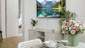 Una zona de menjador moderna amb una taula preparada per a dues persones, un televisor de pantalla plana al mur i un ram de flors decoratiu.