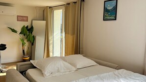 Habitación de hotel con cama, una silla, planta en maceta, cartel en la pared y ventana con cortinas.
