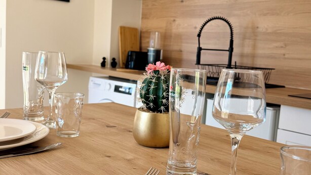 Una mesa de comedor dispuesta con platos, cubiertos y copas de vino, un cactus como centro de mesa y un microondas arriba.