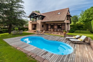 Una casa de dos pisos con piscina, mobiliario de exterior y jardín.