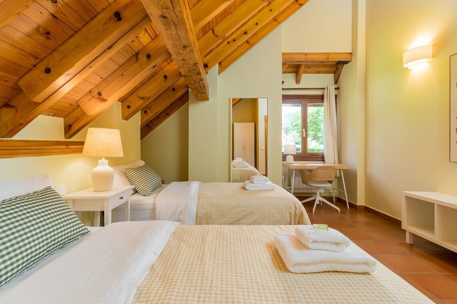 Une chambre avec deux lits, un bureau, une chaise, une lampe et une fenêtre.