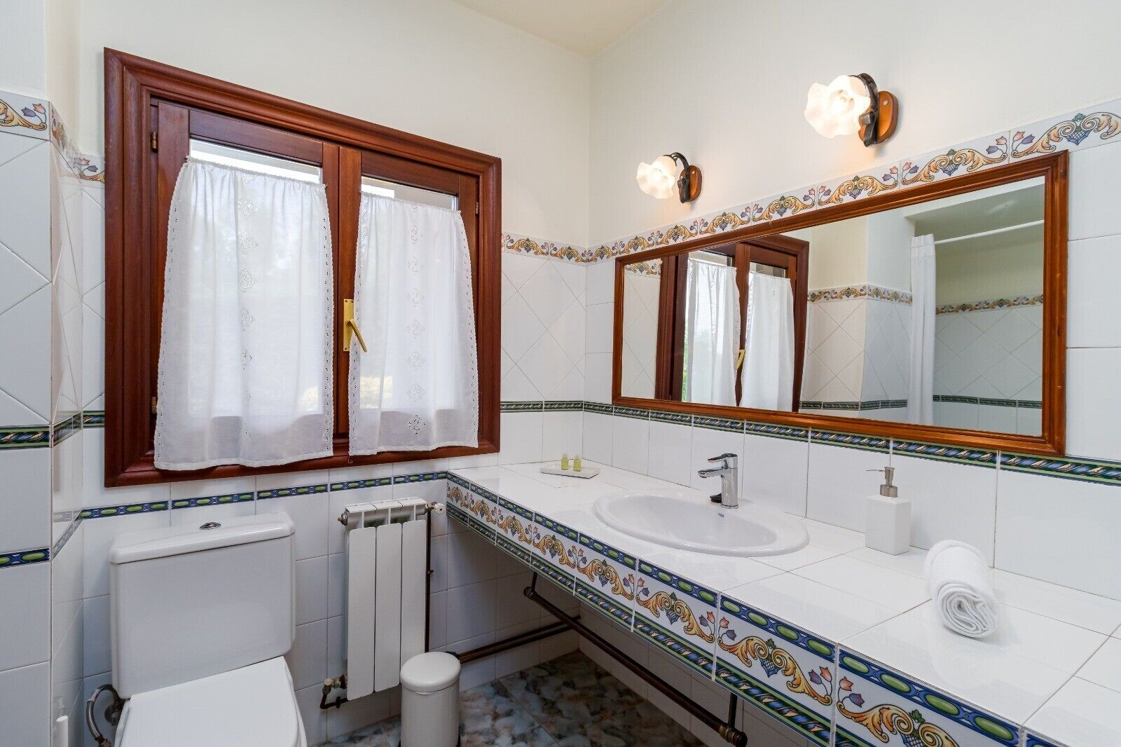 A bathroom with a white sink, a mirror, a toilet, and a window with curtains.