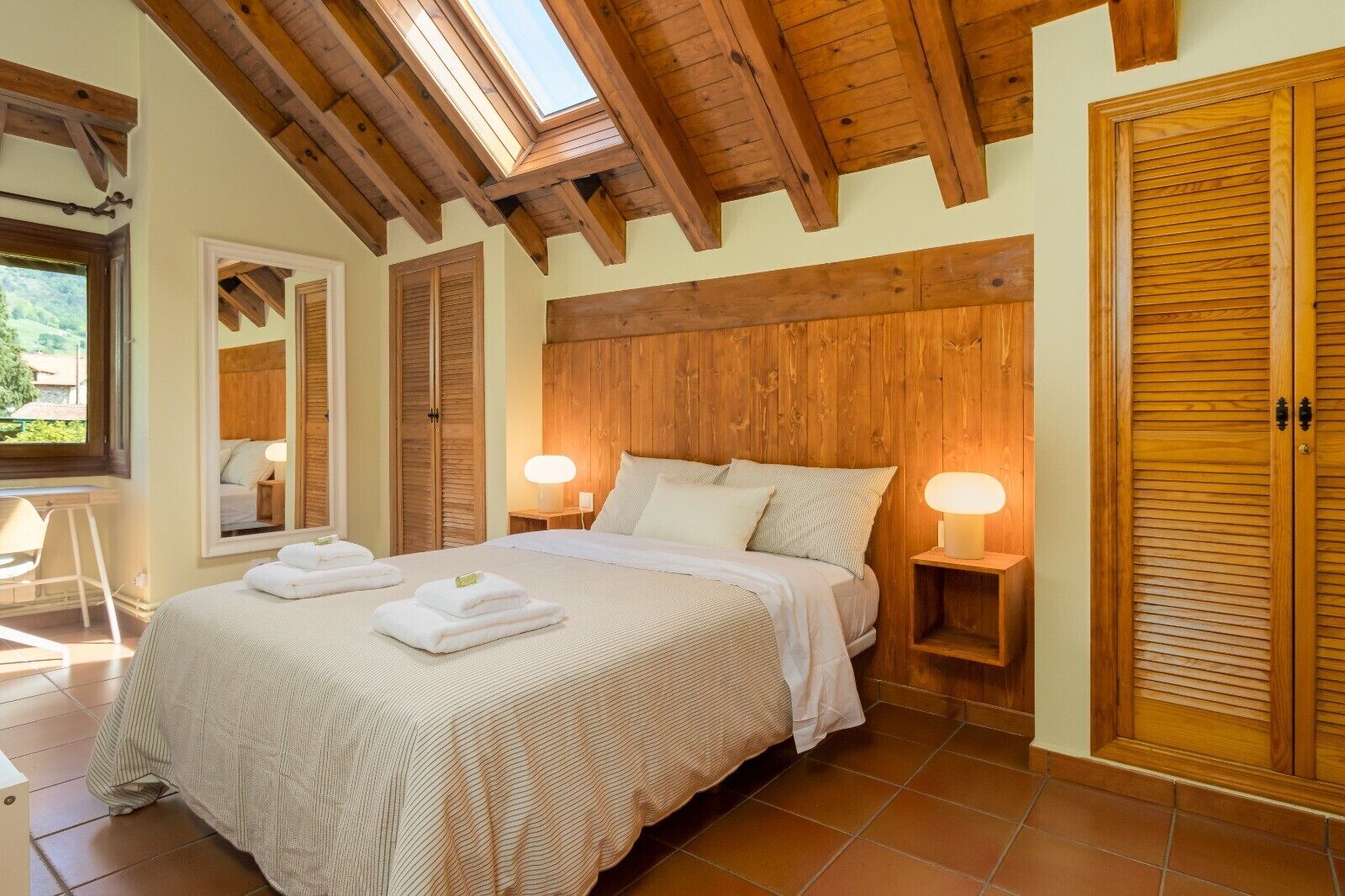 Un dormitorio con techo de madera, una cama grande con ropa blanca, dos lámparas de noche y un armario de madera.