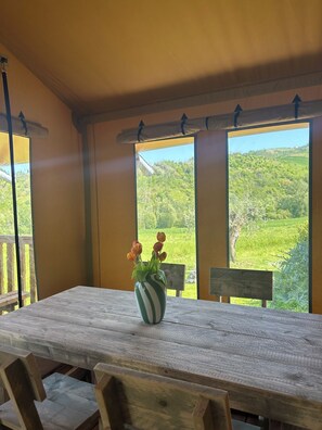 Ein Holztisch mit einer gestreiften Blumenvase, eine Bank und große Fenster mit Blick auf eine grüne Landschaft.