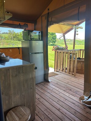 Eine Holzterrasse mit Küchenzeile, inklusive Kühlschrank und Mikrowelle, und Blick auf eine grüne Landschaft.