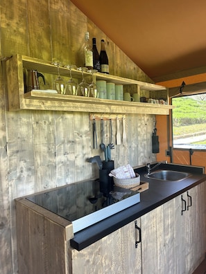 Une cuisine aux murs en bois, dotĂ©e dâun plan de travail noir et dâĂ©tagĂšres oĂč sont rangĂ©es des bouteilles de vin et des ustensiles de cuisine.