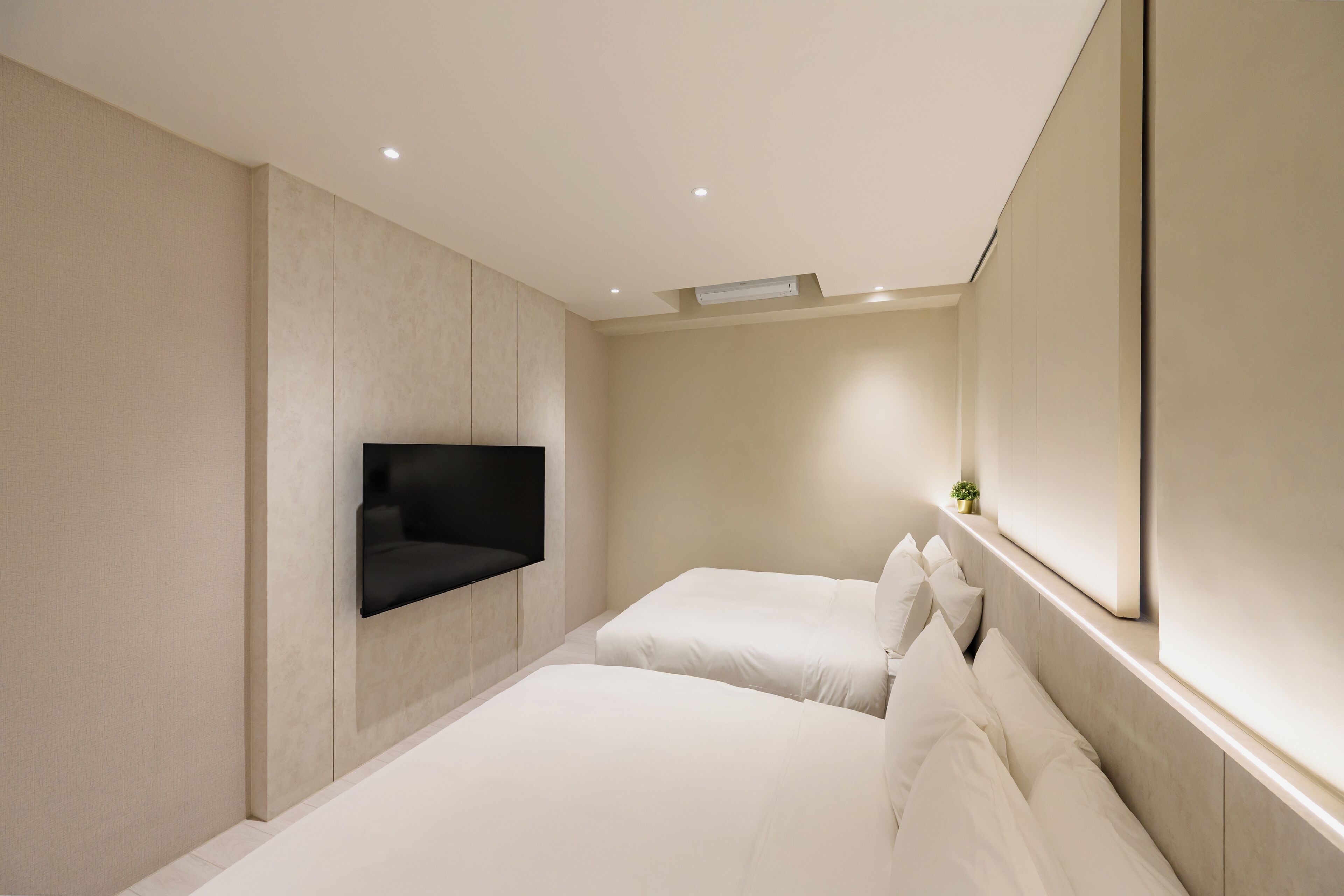A modern hotel room with two beds, a large mirror, and a mounted TV.