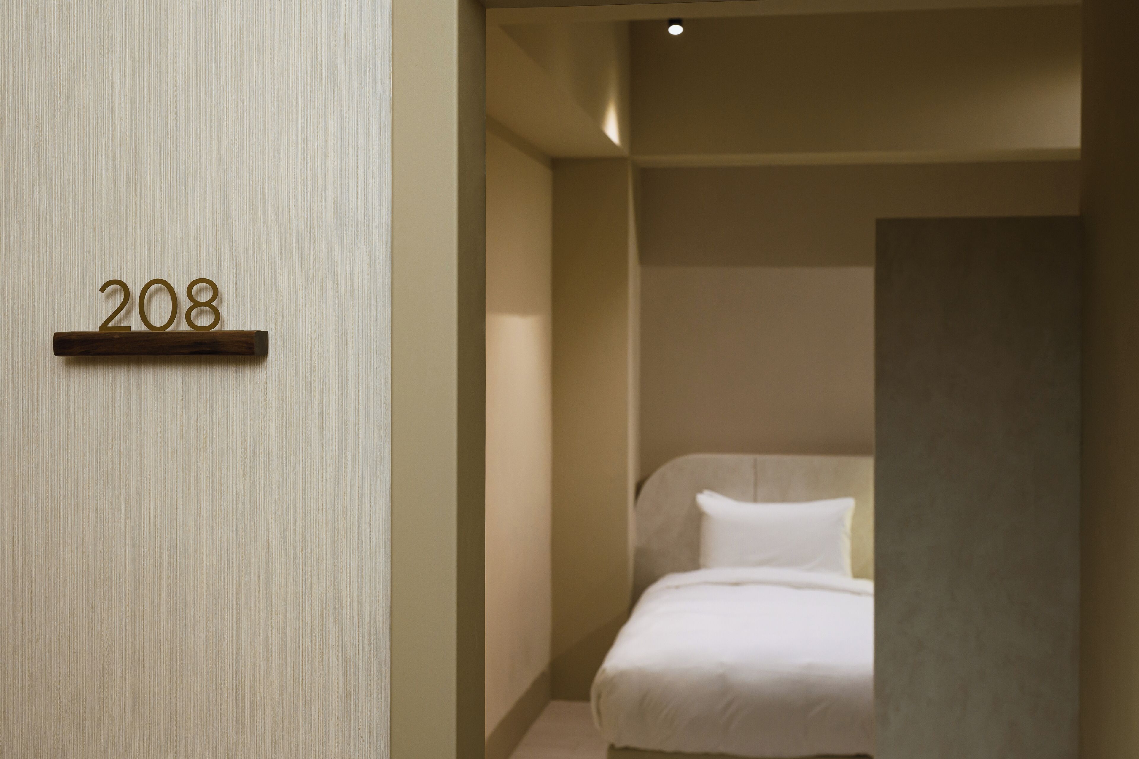 A hotel room with a bed, a wall-mounted number sign '208', and a partial view of a bathroom.