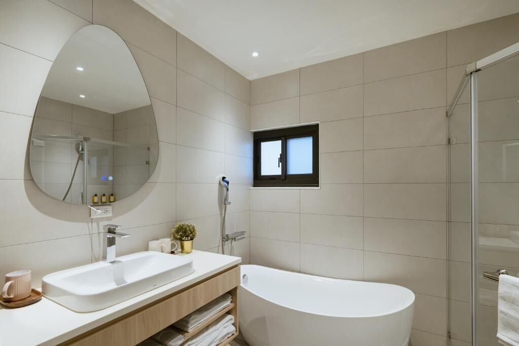 A modern bathroom with a large mirror, a bathtub, a shower, and a small window.
