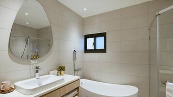 A modern bathroom with a large mirror, a bathtub, a shower, and a small window.