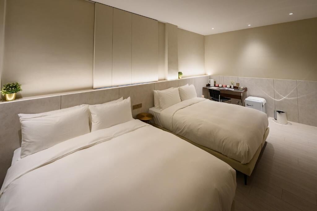 Een moderne hotelkamer met twee bedden, een klein bureau en een nachtkastje met lamp.