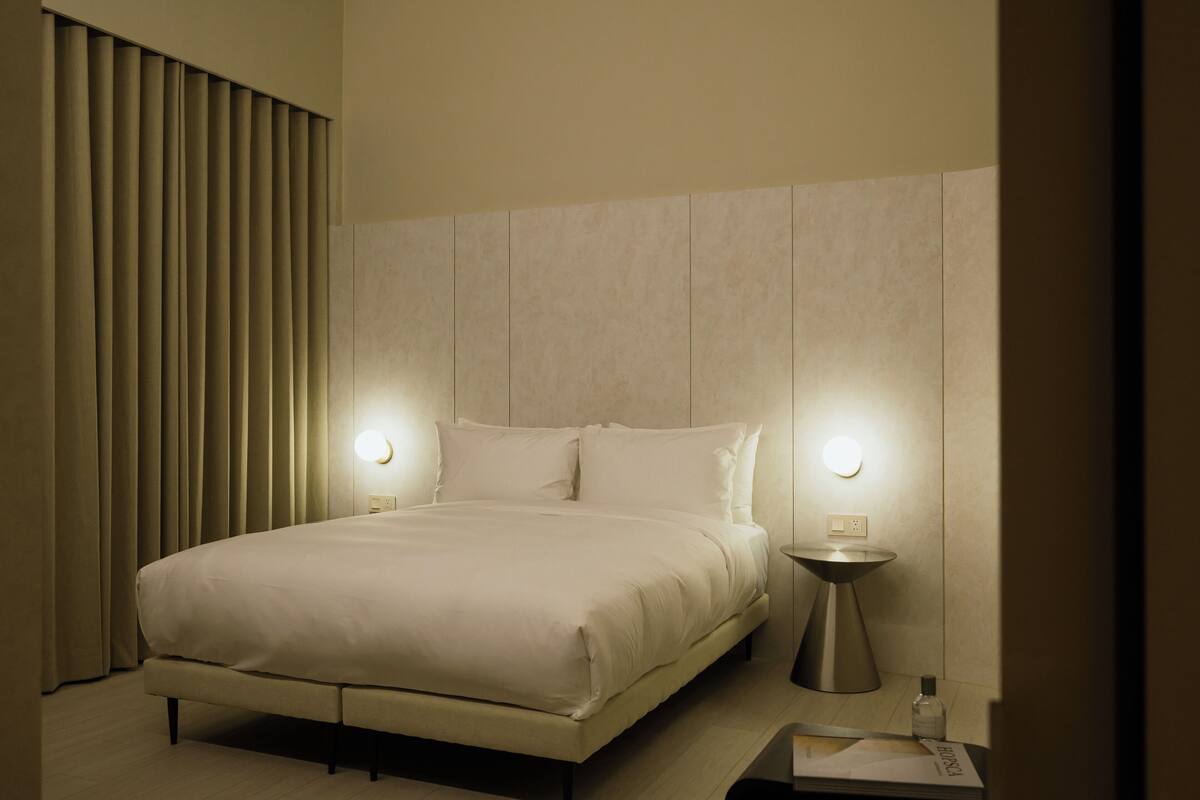 A modern hotel room with a large bed, two bedside lamps, and a bedside table.