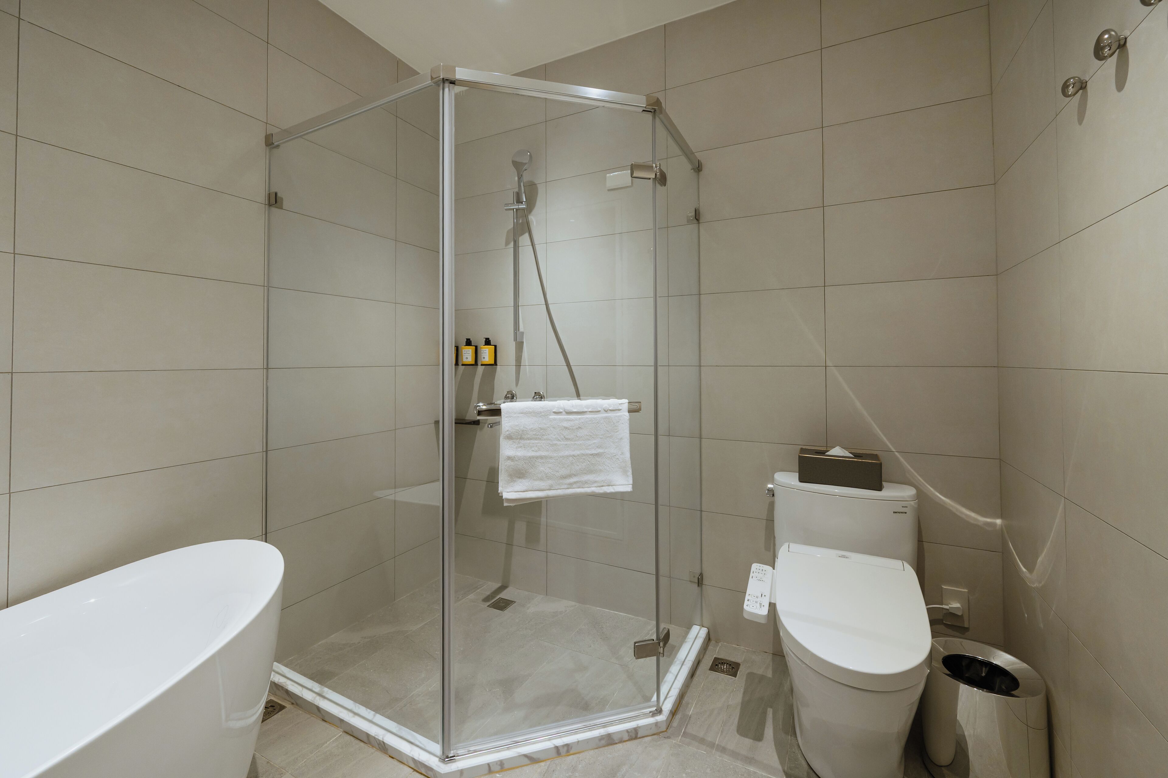 Een moderne badkamer met een douchecabine van glas, een witte badkuip en een toilet.