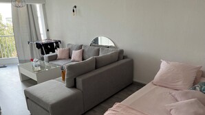 Ett modernt vardagsrum med en grå soffa, ett soffbord i glas och en rosa säng.
