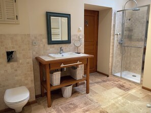 Une salle de bain avec un meuble-lavabo en bois, un lavabo blanc, un miroir, des toilettes et une douche à parois de verre.