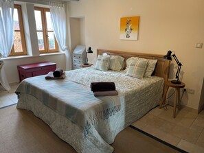 Une chambre bien rangée, avec un grand lit, des tables de chevet, une commode et une fenêtre avec des rideaux.